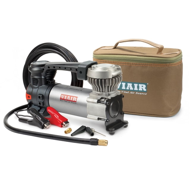 compresor de aire portátil para inflar neumáticos viair 88p 120 psi inflador 12 V plateado, vista 3/4 frontal del compresor con cilindro plateado y cabeza de aluminio con aletas, manómetro integrado, abrazaderas de batería, manguera negra con racor de latón y 3 puntas de inflado; estuche de transporte marrón con logo VIAIR visible; suele usarse también para inflar pelotas y equipos deportivos.