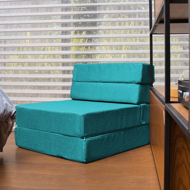 sofá cama plegable - individual -verde petróleo- memory foam sofa cama cozy en posición de silla, color azul petróleo con tapicería textil, respaldo dividido en dos secciones y base acolchada de tres capas con cremallera lateral; vista 3/4 en habitación con persianas y piso de madera, compacto y adecuado como cama individual temporal.