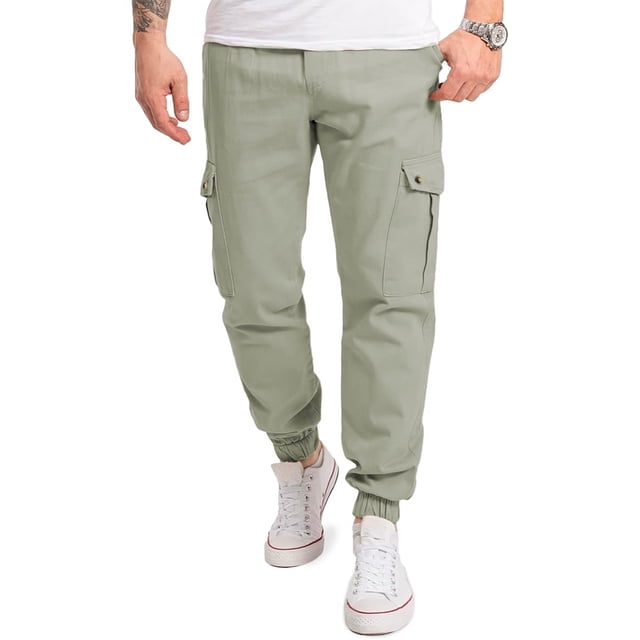 pantalon cargo jogger para hombre shendy vendy slim fit stretch gris, vista frontal 3/4 con modelo de pie; ajuste slim y tiro medio, bolsillos cargo con solapas y botones en muslos, puños elásticos tipo jogger y cordón en cintura; tela de tacto suave según ficha; también suele usarse como opción cómoda para viajes cortos o actividades casuales.