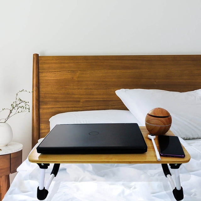 mesa para laptop idea nuova bambú mesa cama mediana con tablero color bambú y patas plegables blancas; vista frontal centrada sobre cama con laptop cerrada, teléfono y accesorio, diseño minimalista y multifuncional ideal para trabajar o desayunar en cama.