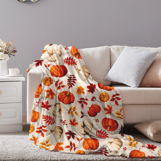 xihbxyly manta de calabaza otoñal, cálida y suave franela 100 x 70 cm drapeada sobre un sofá crema con patrón de calabazas naranjas y blancas y hojas otoñales rojas y amarillas; multiusos para sofá o cama, ideal para ambientar en Acción de Gracias o Halloween, y adecuada también para usar como cobija de viaje ligera.