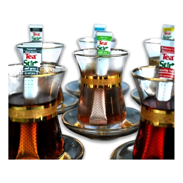 alpont tea stir té negro y avellana, 40 g paquete dentro de infusores individuales en vasos turcos con borde dorado, vista frontal 3/4 que muestra la etiqueta del stick infusionador y el color ámbar del té. Su tamaño compacto lo hace adecuado como opción para preparar té en porciones individuales en la cocina.