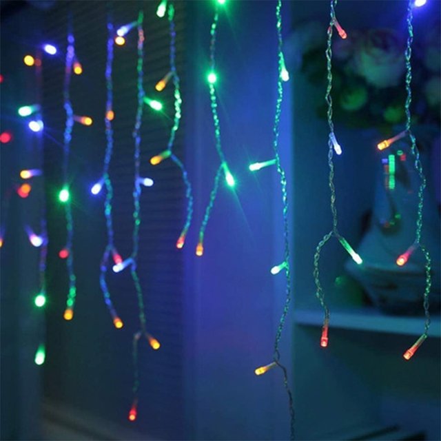 cascada de luces la merced luz led multicolor 500 focos 8 funciones cable transparente 9 m cascada navideña vista frontal de tiras colgantes con focos LED multicolor en cable transparente, efecto cortina en tonos verde, azul, rojo y amarillo sobre fondo interior difuminado; medida 9 m, 120V, 8 funciones y conexión en serie. suele usarse también para ambientar eventos y escaparates.