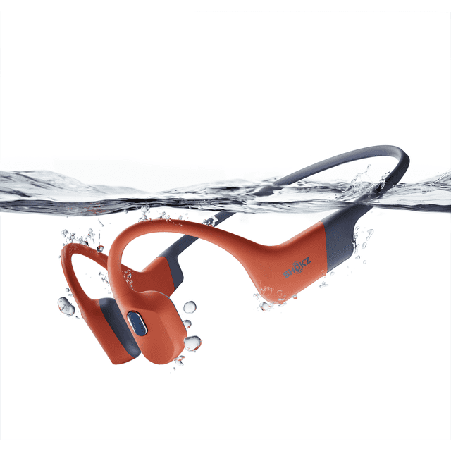 audífonos shokz openswim pro bt + mp3 rojo 3/4 frontal de auriculares rojos Shokz con banda trasera gris parcialmente sumergidos y burbujas; diseño de conducción ósea, botón de modo visible para cambiar Bluetooth o MP3, ajuste ergonómico y delgado pensado para natación y entrenamientos en agua; también suelen usarse para escuchar listas de entrenamiento sin teléfono.