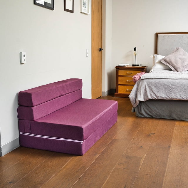 sofá cama matrimonial home memory foam rosa oscuro, vista frontal 3/4 plegado como sofá; tapizado rosa oscuro de tela lisa, respaldo apilable en tres secciones y base con cremallera blanca visible; colocado en habitación con piso de madera junto a cama y buró; versátil, hipoalergénico y con funda removible; a menudo usado como cama compacta para apartamentos.