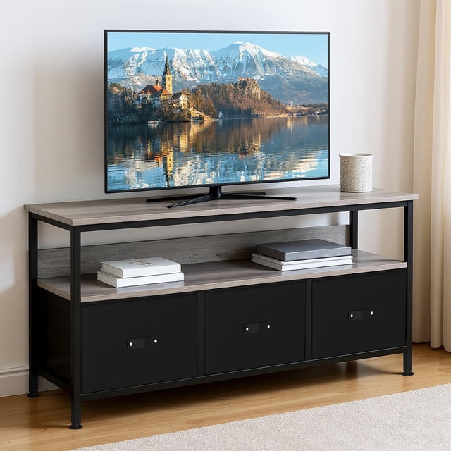 yeshouse soporte de tv con 3 cajones de tela, armario de tv de 55 pulgadas, tablero gris con tela negra en vista frontal: centro de entretenimiento moderno de tres niveles con estructura de metal negro, encimera larga de madera gris, estante abierto y tres cajones de tela negros en la base; televisor sobre la encimera, gestión de cables en la parte inferior y objetos decorativos en el estante. Ideal para almacenamiento multimedia y uso como mueble de entrada por su diseño versátil.