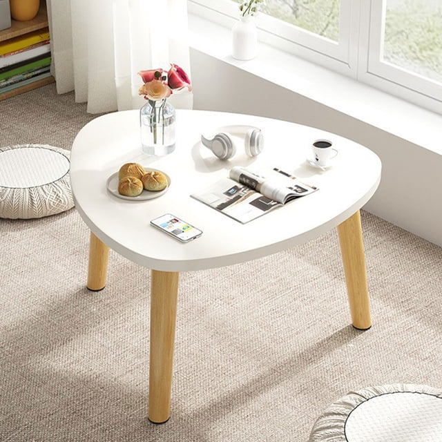 mesa triangular curva de madera para sala de estar mesa de centro triangular curva blanca con superficie curva y esquinas redondeadas, tres patas cónicas de madera natural, dimensiones 40x40x30 cm; vista frontal en piso alfombrado junto a un alféizar con jarrón, audífonos y taza; apta como mesa de té para balcón o mesa de piso para dormitorio.