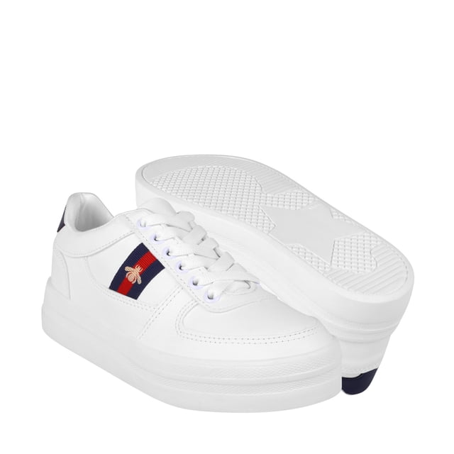 tenis dama stylo 173 simipiel blanco Tenis para dama Stylo en simipiel blanco, vista 3/4 frontal con una zapatilla apoyada y otra mostrando la suela. Silueta casual con cordones blancos, franja azul marino y roja con adorno bordado dorado y suela plataforma altura 4; fondo blanco neutro, ideal para looks urbanos y eventos casuales.