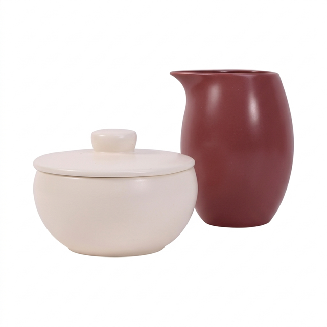azucarera y cremera de 198 ml y 322 ml - crown baccara: vista frontal centrada de conjunto de cerámica con acabado mate satinado; azucarera crema con tapa (198 ml) y cremera terracota con vertedor de precisión (322 ml), siluetas curvas y superficie lisa, a menudo se usa también para servir cremas o jarabes en desayunos y reuniones.
