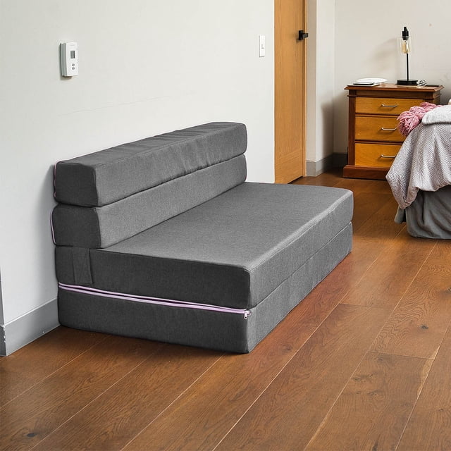 sofá cama plegable -queen size - gris memory foam sofa cama cozy Sofá cama plegable gris en vista frontal 3/4; forma compacta de espuma con funda gris y cierre de cremallera lateral, respaldo plegable que se convierte en cama, silueta baja y líneas rectas, ubicado en dormitorio sobre piso de madera junto a mesita de noche. Versátil para espacios pequeños y a menudo usado como cama adicional para invitados o en estudios.
