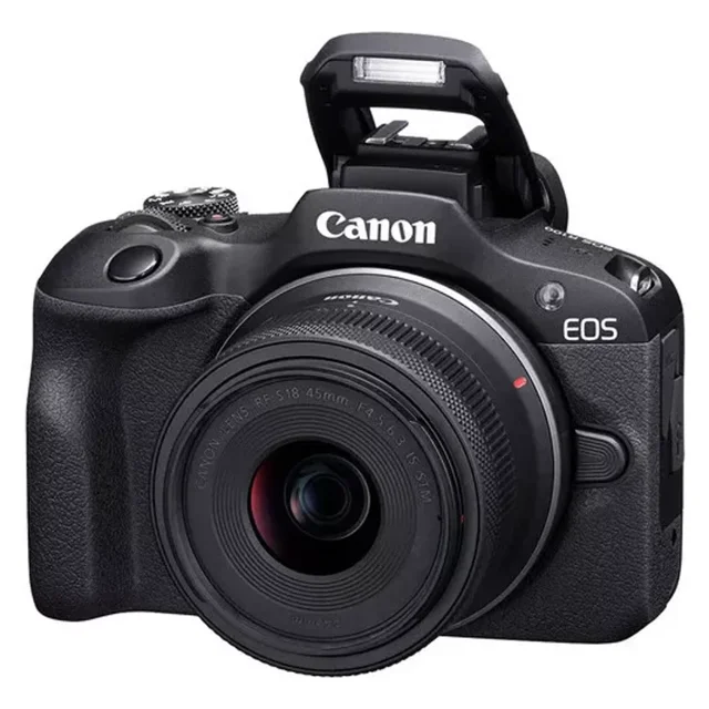 cámara mirrorless canon eos r100 rf-s 18-45mm f4.5-6.3 is stm cámara mirrorless Canon EOS R100 negra, vista frontal 3/4 con flash emergente y lente RF‑S 18‑45mm montada; agarre texturizado, anillo de enfoque y montura RF visibles, pantalla LCD de 3" sugerida en la parte trasera; adecuada para video Full HD 60p y fotografía APS‑C de 24.1 MP, a menudo usada por creadores para vlogs y viajes.