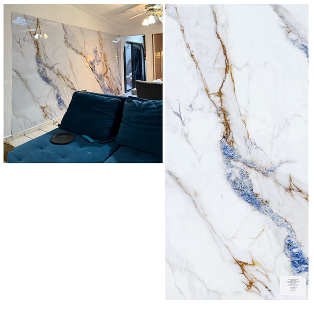 panel decorativo tipo marmol marbella lux pvc homely elegance, revestimiento mural de PVC 240 x 120 cm en sala, vista 3/4 frontal con sofá azul; fondo blanco brillante con vetas doradas y azules, superficie lisa y reflectante, formato ligero fácil de manipular y a menudo usado como respaldo decorativo en paredes interiores.