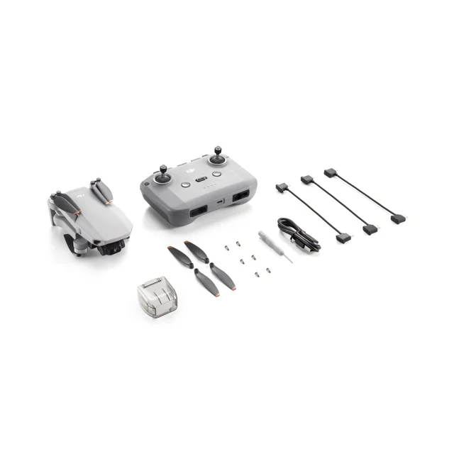 dji mini 2 se dron gris plegado con control remoto y accesorios sobre fondo blanco, vista frontal en 3/4 que muestra la silueta compacta, hélices plegables, cuatro cables de transmisión, cargador y tornillería; pesa menos de 249 g, transmisión de video hasta 10 km y frecuentemente usado para fotografía aérea y viajes.