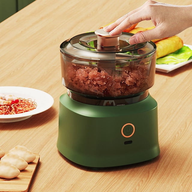 mini procesador de alimentos portátil | picadora de ajo inalámbrica con carga usb en verde: vista frontal centrada de la picadora eléctrica compacta HIGERH (350 ml) con base verde mate y botón frontal, recipiente transparente con tapa y cuchillas visibles; mano presionando la tapa; sobre mesa de madera junto a platos con verduras, ideal para triturar carne, especias y ajo; tamaño compacto adecuado también para preparar salsas pequeñas.