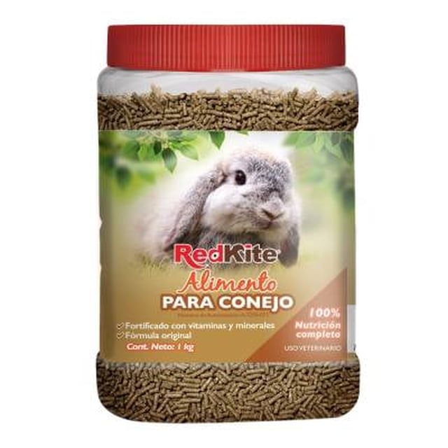 alimento para conejo redkite 1 kg envase con tapa roja, vista frontal de frasco transparente con pellets marrón claro, etiqueta con foto de conejo gris y texto RedKite Alimento PARA CONEJO que menciona 100% nutrición completa y fortificado con vitaminas y minerales; fondo difuminado verde. También suele usarse como premio en sesiones de entrenamiento por su formato en pellets.