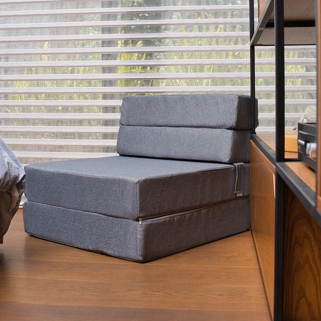 sofá cama plegable - individual - gris memory foam home sofa cama cozy, vista frontal 3/4 de un sofá cama individual gris en posición sofá con respaldo acolchado en dos secciones y asiento plegable de espuma; funda gris con cierre y costuras visibles, sobre piso de madera frente a persiana translúcida en sala contemporánea, tamaño compacto ideal para apartamento y suele usarse también como cama temporal para visitas.