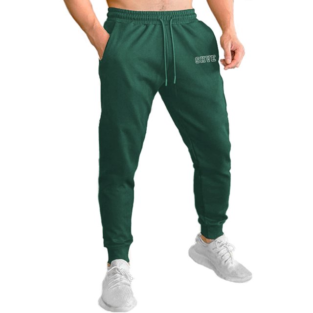 pants jogger para hombre shendy vendy deportivo slim fit elástico en verde oscuro, vista frontal centrada de cintura a tobillo con cintura elástica acanalada y cordón funcional, puños jogger ajustados, bolsillos laterales visibles y logotipo en pierna derecha; adecuado para entrenamiento ligero o uso casual.