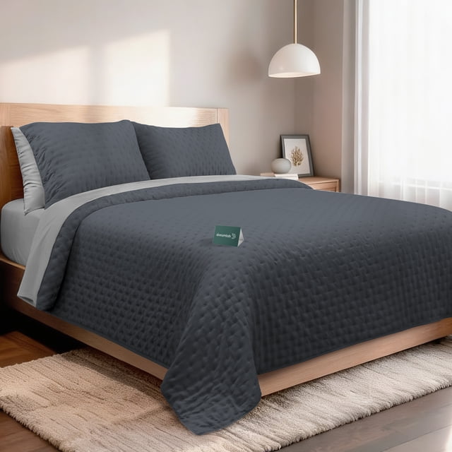 set de 7 piezas edredón ligero y sábanas queen dreamlab, colcha para cualquier temporada, hipoalergénica, diseño trébol grafito, gris. Vista frontal de cama queen con colcha ligera grafito acolchada en patrón trébol y borde gris claro, dos fundas decorativas y sábanas ajustables en microfibra doble cepillado; etiqueta Dreamlab visible, cabecero de madera clara y lámpara colgante en habitación minimalista. Ligera y transpirable, a menudo utilizada para mantener frescura en climas cálidos.