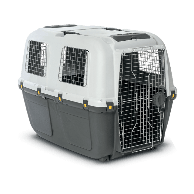 transportadora skudo iata 8 transportadora para perros MPS, vista 3/4 frontal con puerta metálica y ventilas laterales; carcasa plástica bicolor blanco y gris, cuatro cierres de seguridad visibles y asa superior integrada, diseñada para viaje en auto, autobús, barco o avión; también suele usarse como caja de transporte temporal en casa.