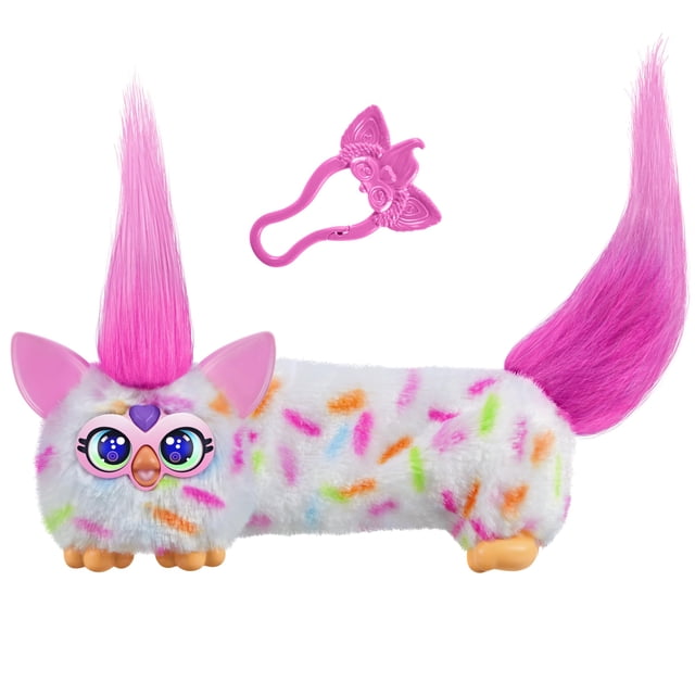 peluche electrónico Furby DJ Furblets Berry-Cup-Cake blanco y rosa, vista frontal centrada de mini juguete con cuerpo alargado y pelaje con motas multicolor; ojos grandes, gema de corazón morada en la frente, orejas y patas rosadas, dos coletas fucsia largas y clip llavero rosa aparte. Estira el cuerpo para activar música, efectos de sonido y frases en Furbish; también suele usarse como juguete de viaje por su clip extraíble.