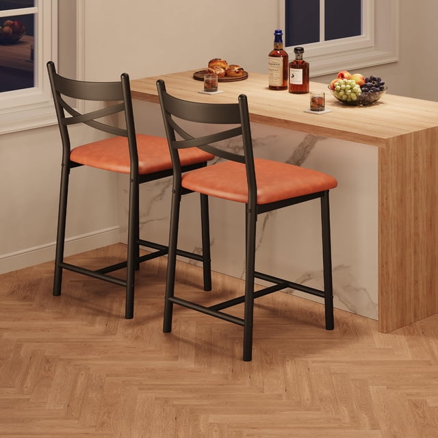 yeshouse taburede barra de altura conjunto de 2/4, silla de comedor de imitación de cuero con respaldo y cojín grueso para la isla de la cocina, barra de mostrador — par de taburetes marrón retro con asiento acolchado tapizado en piel sintética y respaldo ergonómico con refuerzo en X; estructura metálica negra y reposapiés integrado, vista 3/4 frente a isla de cocina de madera. Su tamaño compacto los hace adecuados también para estaciones de trabajo pequeñas.