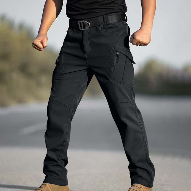 ceisia men's lined cargo hiking pants, waterproof with multiple pockets for winter gift outdoor skiing Vista frontal de pantalones negros para senderismo con forro; silueta recta con rodillas articuladas, costuras reforzadas y trabillas para cinturón. Bolsillos cargo con solapa, bolsillos con cremallera en muslo y bolsillos laterales visibles en tela resistente al agua. Fondo exterior desenfocado; también suelen usarse como pantalones funcionales para actividades de montaña o viaje.