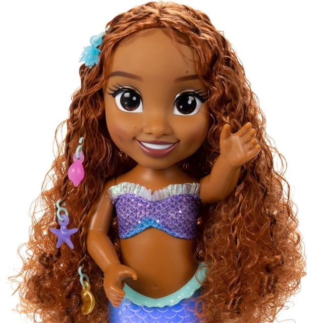 jakks ariel sirenita live action 11 pulgadas muñeca Ariel de 11 pulgadas, vista frontal centrada; cabello largo rizado castaño, top tipo concha morado con textura escamada y falda azul claro con cinturilla decorativa, brazo derecho levantado, fondo blanco. Apta para exhibir en estanterías de muñecas y para juegos de vestir.