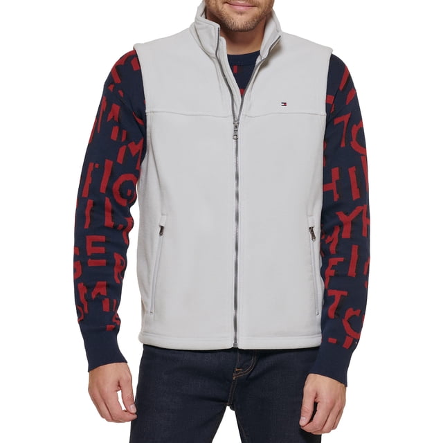 chaleco tommy hilfiger de forro polar ice para hombre, para exteriores Chaleco sin mangas Ice color gris en vista frontal centrada, forro polar suave, cuello alto y cierre de cremallera completo, bolsillos laterales con cierre y logotipo Tommy Hilfiger bordado en el pecho; modelo lleva suéter debajo en talla mediana, uso versátil para actividades al aire libre y salidas casuales, a menudo usado como capa intermedia ligera.
