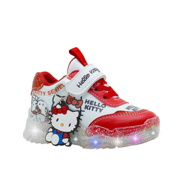 tenis luces led para niña gatito moda color blanco rojo rojo 20 Pequenos Pasos — Tenis deportivos para niña en blanco y rojo con cierre de velcro "Hello Kitty", cordones elásticos, refuerzos sintéticos en puntera y talón, suela transparente con luces LED que se activan al caminar y colgante decorativo de gatito; vista 3/4 frontal sobre fondo neutro, aptos para escuela o parque y también usados para actividades recreativas infantiles.