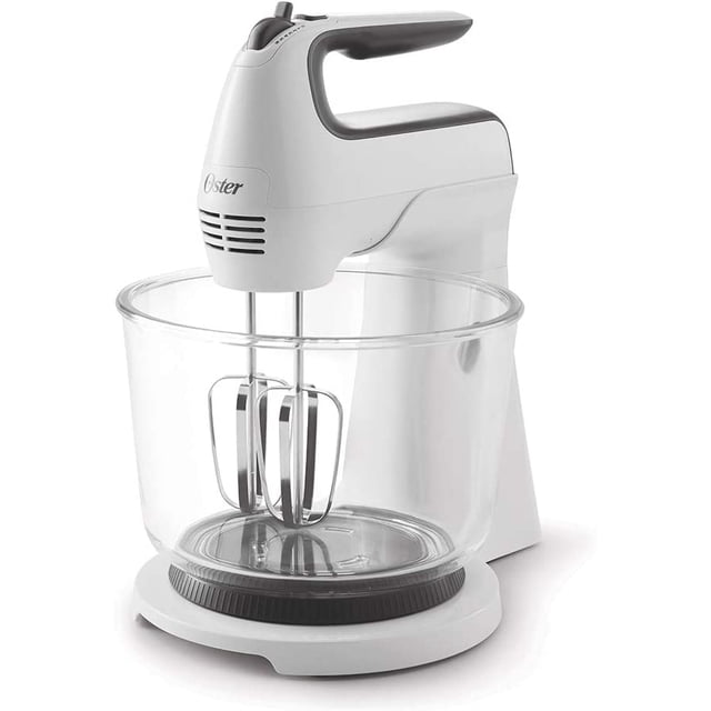 batidora pedestal oster 2121775 6 velocidades con tazón de vidrio blanco — vista frontal 3/4 de la batidora pedestal blanca con cabezal desmontable y mango ergonómico; tazón de vidrio transparente de 3.7 L con dos batidores metálicos instalados, perilla superior para seleccionar 6 velocidades y turbo, base con soporte giratorio y marca Oster visible; ideal para mezclar masas y merengues y también usada como batidora de mano para preparaciones pequeñas.