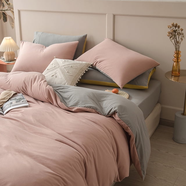 juego de cama de 4 piezas para dormitorios | poliéster suave lavado reversible: toma 3/4 frontal de funda nórdica rosa por fuera y gris por dentro sobre sábana ajustable gris y 2 fundas de almohada rosas; textura lisa y caída suave, ambiente minimalista con mesita y lámpara. Suele usarse para renovar rápido habitaciones de invitados.