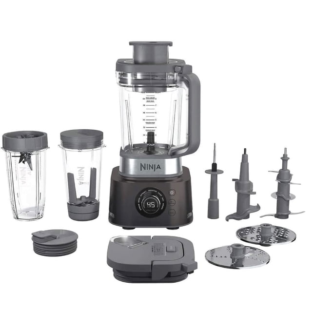 licuadora con procesador 1200 watts ninja co401b plateada, vista frontal centrada con base digital y dial, jarra XL transparente con mango y tapa, vaso extractor y vaso para llevar con tapas, tres cuchillas desmontables, accesorios de procesador y discos ralladores visibles; indicada como procesador de alimentos y extractor de nutrientes, también apta para preparar porciones individuales para llevar.