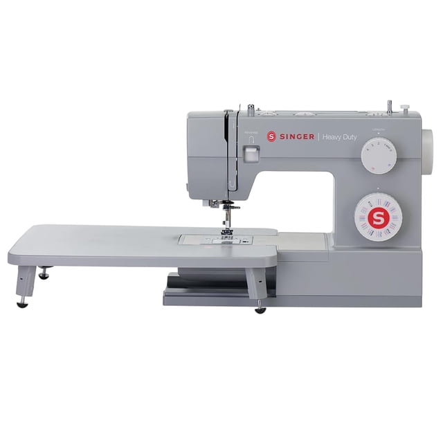 máquina de coser singer heavy duty 6380 con mesa extensible gris, vista frontal 3/4 con mesa extensible acoplada; cuerpo metálico con dial selector de puntadas grande, logo S rojo, palanca de prensatelas y enhebrador integrado visibles; área de aguja con placa expuesta y luz LED; motor potente indicado para telas gruesas y también adecuada para acolchar piezas pequeñas.