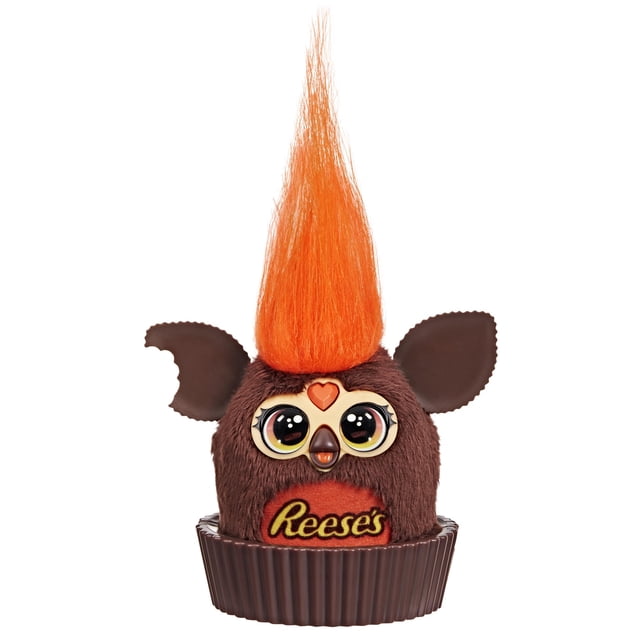 furby furblets reese's peanut butter cup mini peluche electrónico de 3 pulgadas, Furby multicolor de 3" con pelaje marrón, mechón naranja puntiagudo, orejas marrón, ojos grandes estilo caricatura, nariz pequeña y logo Reese's en base tipo molde de cupcake; también usado con fines decorativos en estanterías.