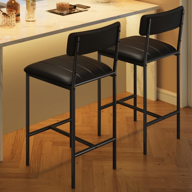 yeshouse juego de 2 sillas de comedor juego de 2 sillas tapizadas negras en PU con asiento y respaldo acolchados, estructura metálica negra y tapa de tablero MDF según especificaciones; vista 3/4 lateral junto a barra alta en cocina, diseño compacto apto para apartamento y a menudo usadas como taburetes de bar para espacios pequeños.