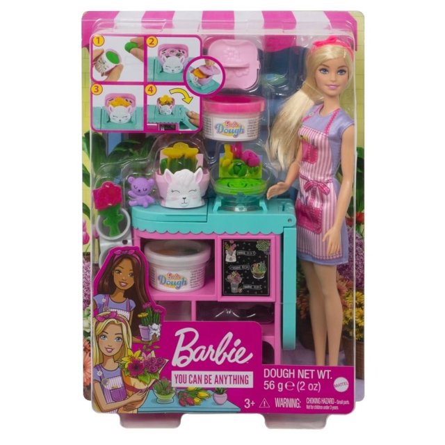 muñeca barbie careers tienda de flores Vista frontal del set en empaque; muñeca Barbie con delantal rosa a rayas, estación turquesa para crear flores con masa en tres colores, dos jarrones, molde, herramienta de limpieza y oso de peluche. Escena de tienda ilustrada al fondo; ideal también para juegos de role‑play, recomendado 3+ años.