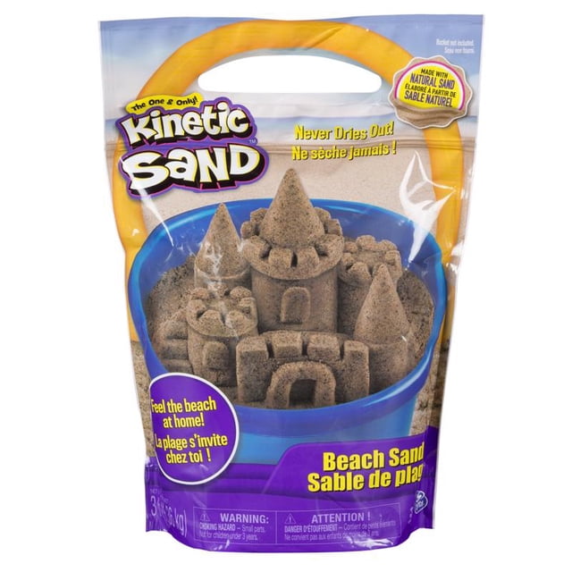 arena de playa natural kinetic sand spin master, 1 paquete de 1,42 kg empaque frontal con asa; saco transparente y morado que muestra arena cinética color natural compactada en un castillo dentro de un balde azul, logotipo Kinetic Sand visible, texto del producto y marca en la parte inferior, tamaño 48 oz, ideal para modelado y manualidades para mayores de 10 años.
