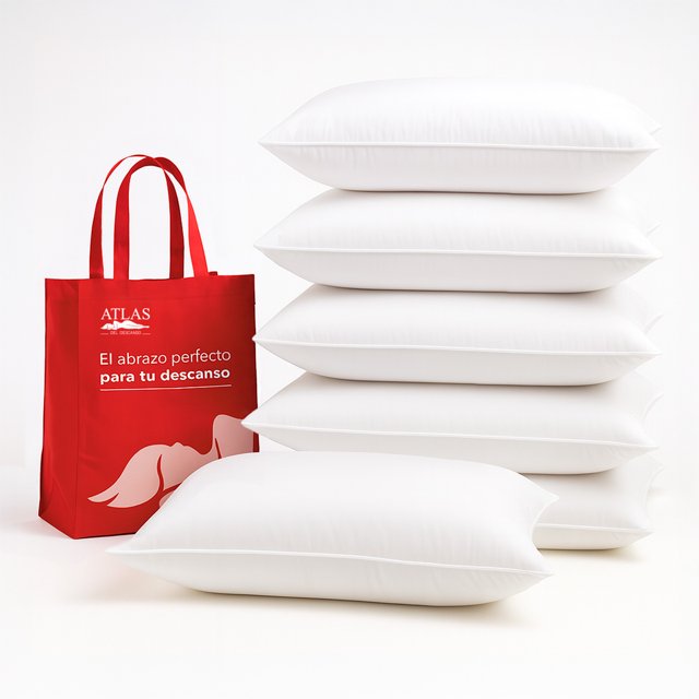 set 6 almohadas suaves confortables para cama hogar hotel. Vista 3/4 de seis almohadas blancas estándar apiladas y una en primer plano; fundas lisas blancas con costura perimetral y relleno de fibra de poliéster que mantiene la forma, junto a una bolsa roja con logo Atlas del Descanso sobre fondo claro. Adecuadas para hogar, hoteles, Airbnb y camas individuales, matrimoniales y queen; también suelen usarse para decorar habitaciones de huéspedes.