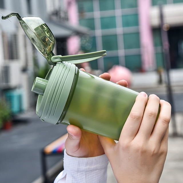 food grade protein shaker cup | high temp resistant plastic | built-in stirring mixer | leak-proof lid | 700ml large capacity | odorless durable bottle | for fitness hydration | green pink black Verde RAXION food grade protein shaker cup en verde, vista 3/4 sostenida por dos manos; cuerpo translúcido de polipropileno 700 ml, tapa roscada con cierre abatible y anillo de silicona a prueba de fugas, mezclador de tornillo integrado visible, tamaño 9x9x23,5 cm (3,54x3,54x9,25 in). Apto para batidos de proteína y uso en viajes.