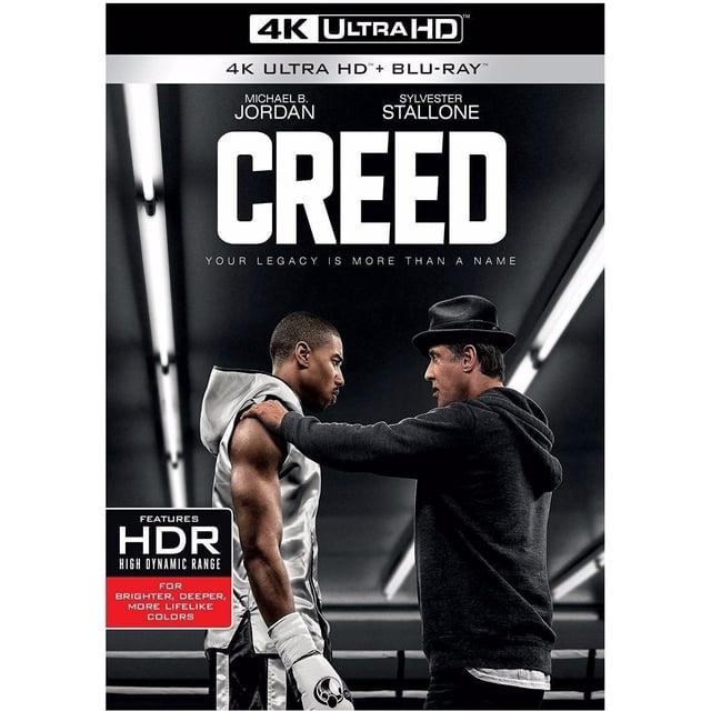 creed sylvester stallone pelicula 4k ultra hd + blu-ray + dc warner bros 4k ultra hd — Carátula frontal centrada con vista 3/4 de un boxeador con capucha sin mangas a la izquierda y un entrenador con sudadera y gorra a la derecha tocando su hombro; título grande "CREED" arriba, banner superior "4K ULTRA HD + BLU-RAY" y sello HDR en la esquina inferior izquierda, fondo de gimnasio con luces lineales.