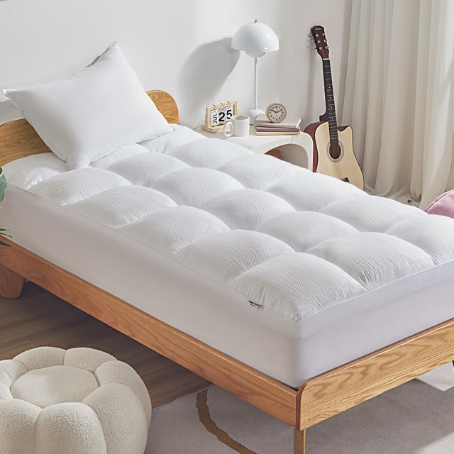 cubrecolchón sleep zone, tamaño doble, extra grueso, blanco — Vista frontal en 3/4 de un cubrecolchón doble blanco extra grueso con acolchado en cuadros y superficie de fibras ultrafinas cepilladas; falda elástica profunda que envuelve el colchón (ajusta 8 a 21 pulgadas) y etiqueta Sleep Zone visible; fondo de dormitorio con mesa de noche y guitarra; a menudo usado para añadir suavidad a colchones firmes.