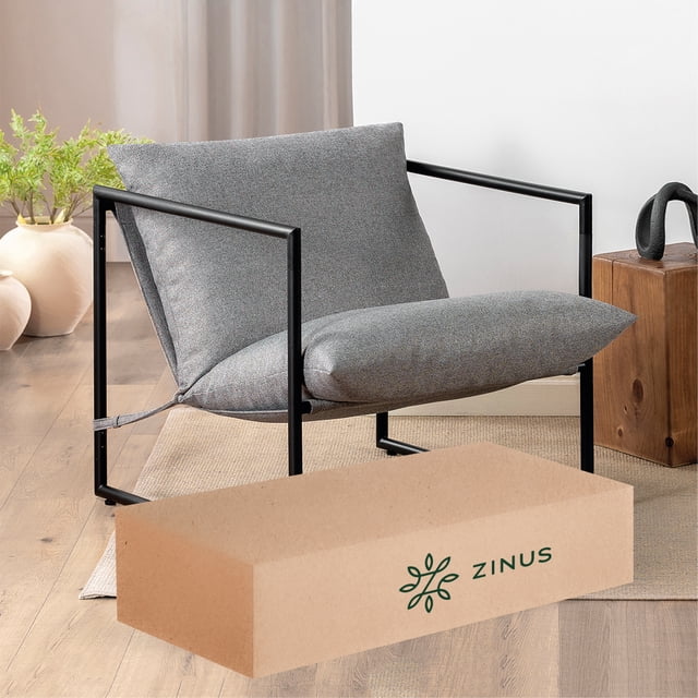 silla de metal zinus aidan con cojines de memory foam color gris claro silla 3/4 frontal con estructura de acero negro y silueta cuadrada; cojines gris claro rellenos de espuma triturada (memory foam según título), respaldo independiente y asiento acolchado; apoyabrazos en marco abierto y base de patas rectas; situada sobre piso de madera junto a caja de envío Zinus. Incluye piezas y herramientas para armar en 30 min; adecuada como asiento adicional en sala o estudio.
