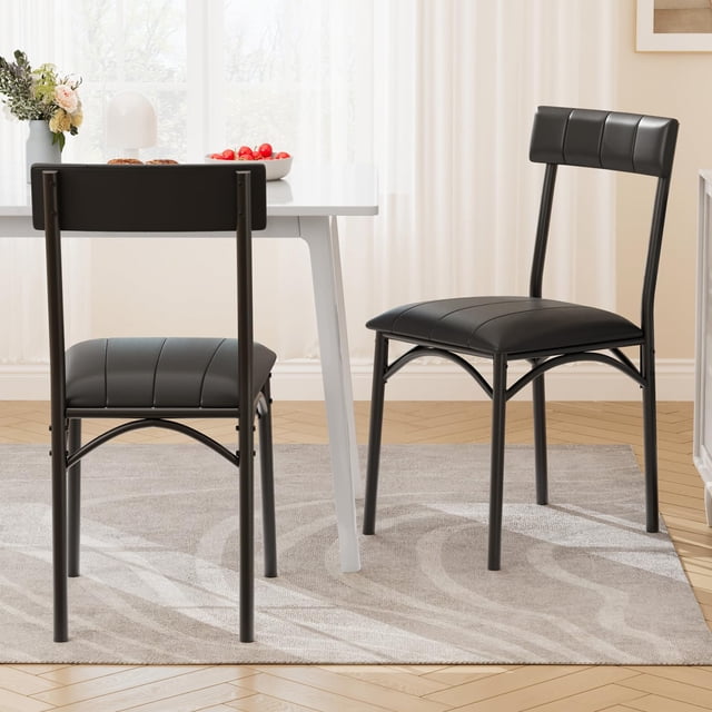 yeshouse juego de 2 sillas de comedor, sillas tapizadas de cuero sintético negras con estructura metálica resistente, asientos y respaldos acolchados con costuras verticales, vista frontal y lateral junto a mesa blanca en comedor luminoso; aptas para cocina, comedor o apartamento y también usadas como sillas extra para oficina en casa.