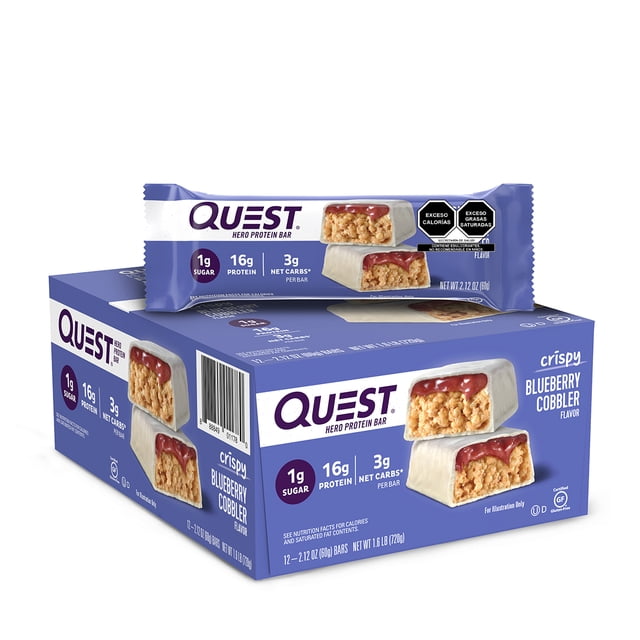 quest hero barra sabor a postre de mora azul caja con 12 barras; vista frontal en ángulo con una barra individual sobre la caja. Envase violeta y blanco muestra barra crujiente con cobertura roja, rótulos que indican 1 g azúcar, 16 g proteína y 3 g net carbs; caja sobre fondo blanco. Adecuada como snack proteico para llevar.