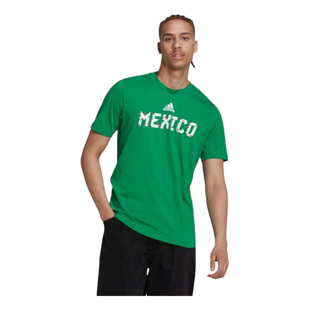 playera adidas hombre mexico copa mundial fifa 2022 verde s frontal centrada, camiseta verde de manga corta y cuello redondo con estampado 'MEXICO' en blanco y logo adidas sobre el pecho; tejido jersey suave visible en ligeras arrugas, modelo de pie con manos en bolsillos sobre fondo blanco; adecuada para uso casual y a menudo usada como prenda de viaje ligera.