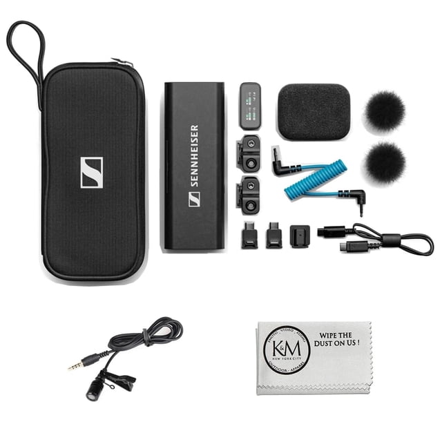 sistema de audio inalámbrico sennheiser profile para 2 personas con micrófono — vista cenital del kit: estuche negro con logo, barra de carga rectangular con logo Sennheiser, dos transmisores lavalier con clip y grabación integrada, dos protectores de espuma y dos pelotas antiviento, cable TRS, cable USB-C y varios adaptadores, más paño de microfibra; diseñado para grabación móvil y adecuado para entrevistas en exteriores.