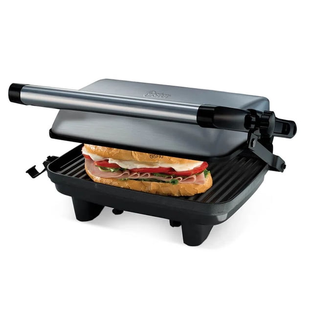 sandwichera oster ckstpa2880-013 panini grill plateado, vista 3/4 frontal con tapa levantada y un sándwich en las placas; placas antiadherentes ranuradas superior e inferior, mango tubular de acero, bisagra con sistema de altura ajustable para distintos grosores de pan, área para enrollar cable y diseño compacto para almacenamiento vertical.