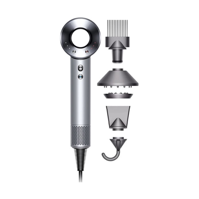 dyson - supersonic hair dryer - white/silver Secador de pelo blanco y plateado, vista frontal con mango cilíndrico y orificio circular en la cabeza; botones de velocidad y rejilla de ventilación en la base; cinco accesorios magnéticos a la derecha: peine Flyaway, difusor redondeado, boquilla ancha, boquilla estrecha y gancho. Diseñado para secado ultrarrápido y control de calor inteligente; también suele usarse para peinados de viaje por su tamaño compacto.