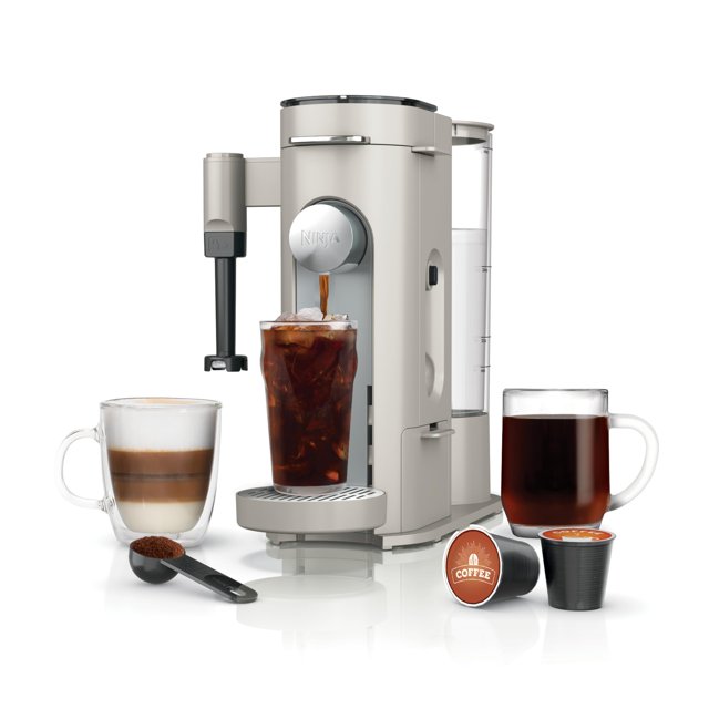 cafetera de una sola porción ninja pod & grounds, compatible con cápsulas k-cup, prepara molidos, diseño compacto, espumador de leche incorporado, 56 oz. depósito, 6 oz. taza a 24 oz. tamaños de taza, vista frontal centrada de la cafetera gris Ninja con depósito trasero transparente de 56 oz. y boquilla frontal con logo sirviendo café sobre hielo; espumador lateral, bandeja de goteo y cajón de almacenamiento visibles; cápsulas K‑Cup, cucharita medidora con posos y tazas de muestra al frente. Adecuada para preparar concentrados y bebidas estilo cafetería en casa.