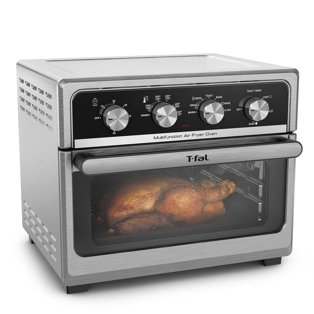 t-fal 9 in 1 toaster oven air fryer combo stainless steel convection countertop oven, fast heatup, 7 pound chicken capacity, extra crispy results, toast, bake, air fry, reheat, broil — Vista frontal en tres cuartos de un horno freidora de aire T-fal en acero inoxidable con panel negro y tres perillas cromadas, puerta de vidrio que muestra un pollo rostizado de hasta 7 lb en la parrilla central, acabado cepillado, laterales ventilados y asa tubular; también suele usarse para tostar y recalentar porciones rápidas.